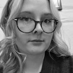 Mustavalkoinen kuva jossa tyttö jolla silmälasit ja vaaleat kihartuvat hiukset