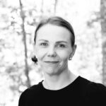 Hymyilevä naisoletettu jolla ruskeat kiinni olevat hiukset. Päällä musta paita.