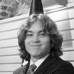 Musavalkoinen kuva jossa hymyilevä poika, jolla ruskeat kihartuvat hiukset