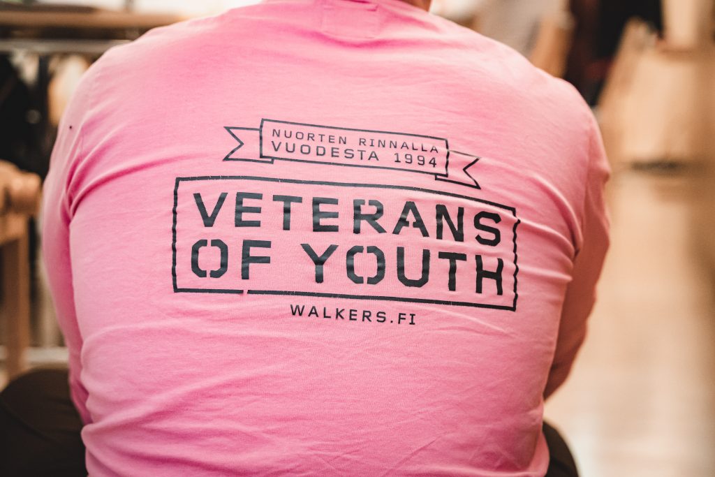 Kuva henkilön selästä, jossa pinkissä t-paidassa lukee "veterans of youth"