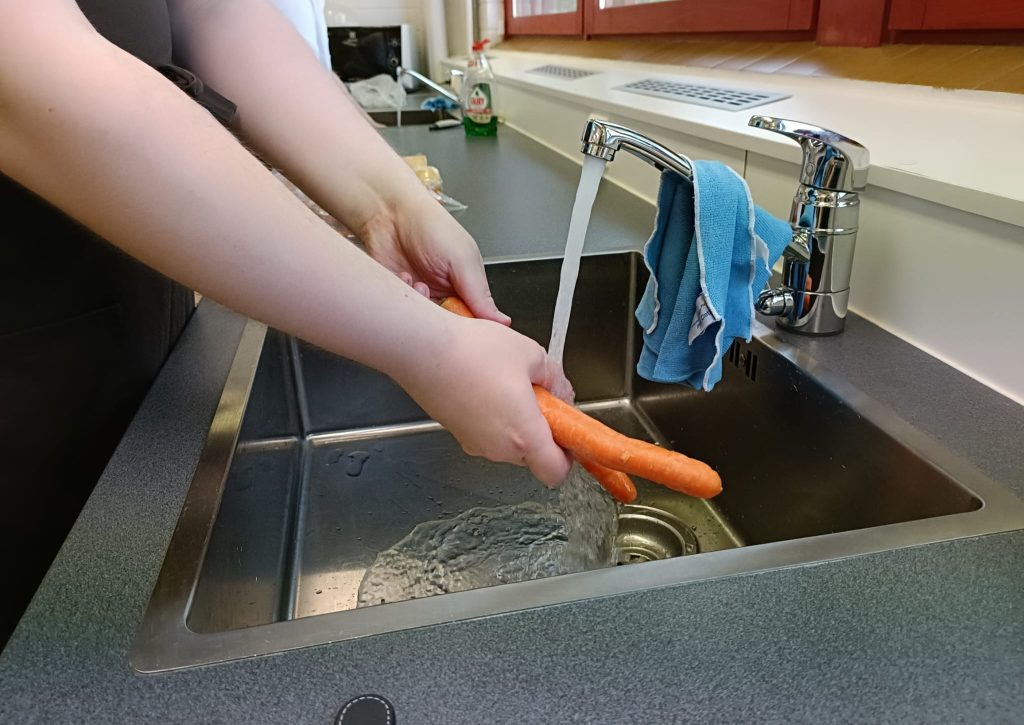 Kuvassa nuoren kädet. Nuori pesee teräksisessä altaassa porkkanaa