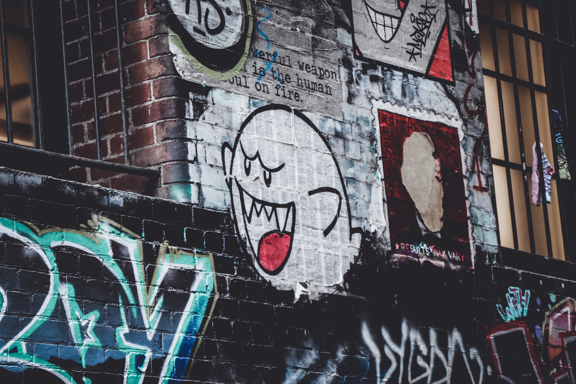 tummalla rähjäisellä graffitiseinällä erilaisia tekstejä ja kuvia sekä spraymaalattu vaalea videopelin virnuileva haamu