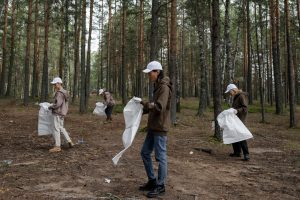ryhmä vapaaehtoisia on kokoontunut mäntymetsään keräämään roskia vaaleisiin roskapusseihin