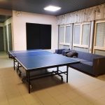 Kuvassa Kurkimäen Pop-up nuokkarin sisätiloista otettu kuva. Tilassa on sininen pingispöytä, siniset sohvat, valkoiset laattalattiat ja valkoiset seinät. Oikealla seinustalla ikkunoita ja vaaleat verhot. Takaseinällä musta neliskanttinen elementti seinällä.