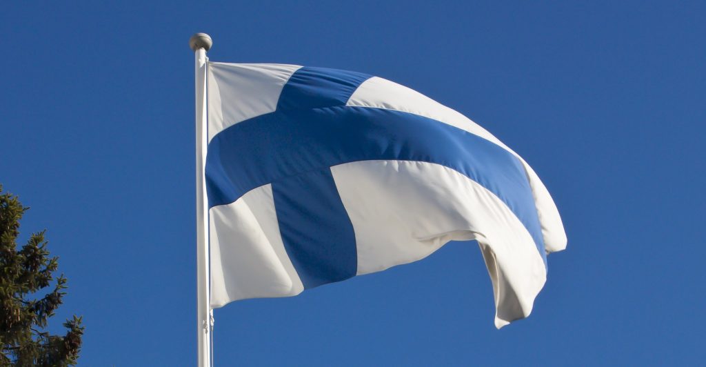 Suomen lippu heiluu tuulessa sinistä taivasta vasten.