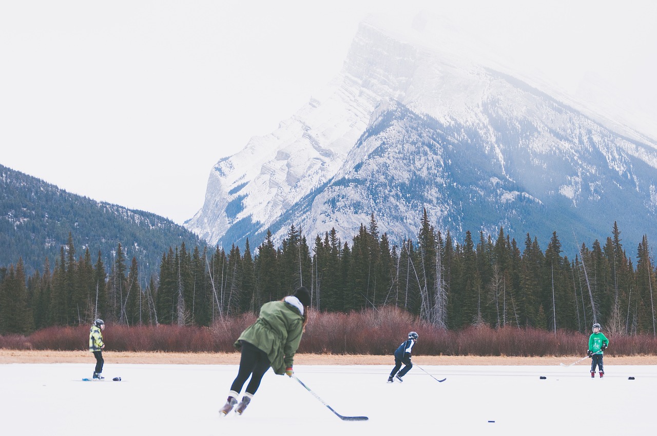 Nuoret pelaavat jääkiekkoa luistelukentällä. Taustalla iso vuori ja puita.
