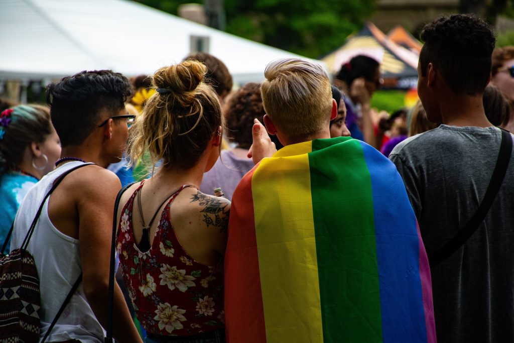 Ihmisjoukko pride tapahtumassa ja yhdellä ihmisistä pridelippu selässä
