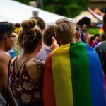 Ihmisjoukko pride tapahtumassa ja yhdellä ihmisistä pridelippu selässä
