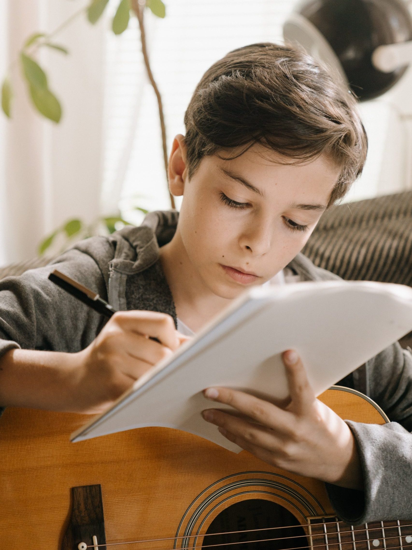 Nuorella kitara sylissä ja kirjoittaa paperille