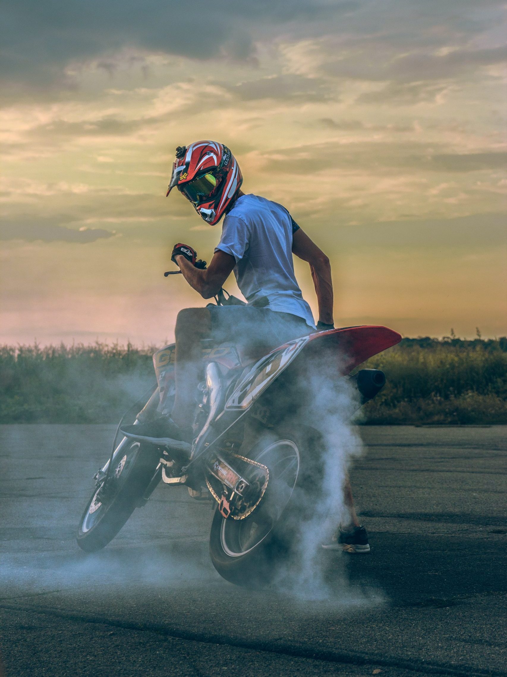 Nuori polttaa mopon kumia taajamassa päässään punasävyinen kypärä ja keltaisena heijastavat ajolasit. Avainsanoja: mopo, paja, liikenne, turvallisuus, ajokortti, mopokortti