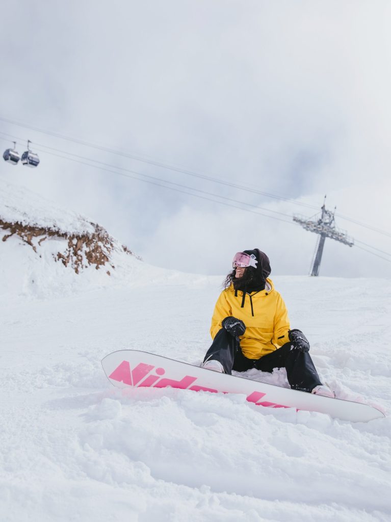 Nuori on lumilautailemassa ja on istahtanut maahan laskettelumäessä. Avainsanoja: talvi, loma, hiihtoloma, laskettelu, lumilautailu, retki, ilo, liikunta, ympäristö