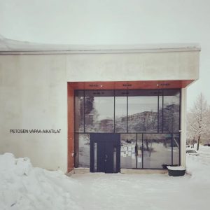 Petosen vapaa-aikatilat. Valkoinen rakennus, iso lasiseinä, jossa tummanharmaa, metallinen pariovi. Lunta maassa ja katolla.