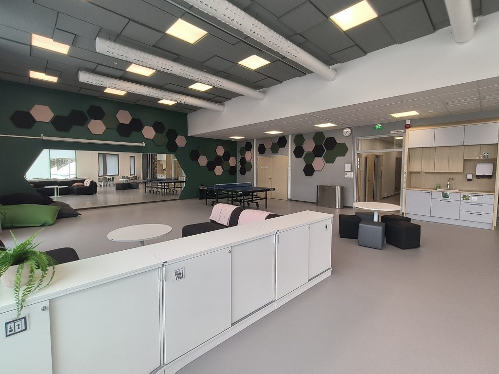 Jynkän nuorisotilan olohuone. Olohuoneessa on valkoiset matalat kaapit ja pingispöytä. Lattia on harmaa ja takaseinä on vihreä.