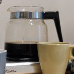 Kahvinkeittimellä on keitetty kahvia ja keittimen edessä on kolme mukia.