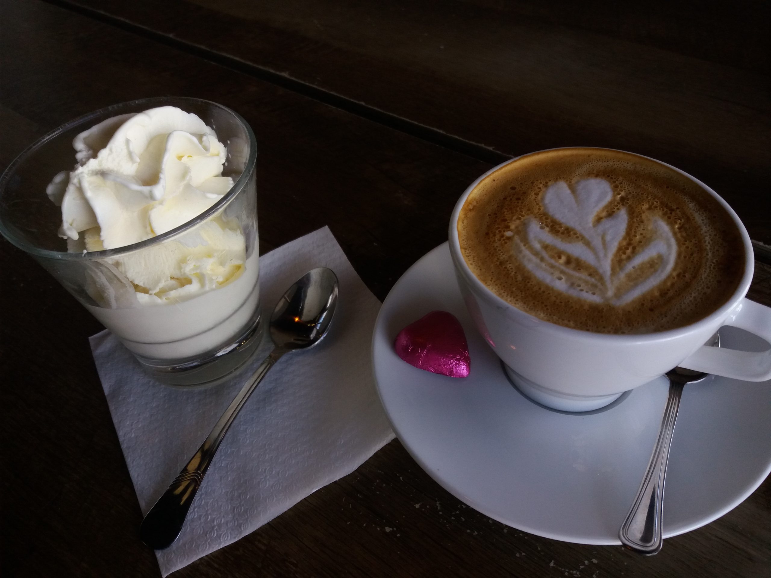 Kahvilan kuviokahvi ja pieni jäätelökippo, tumalla pöydällä.