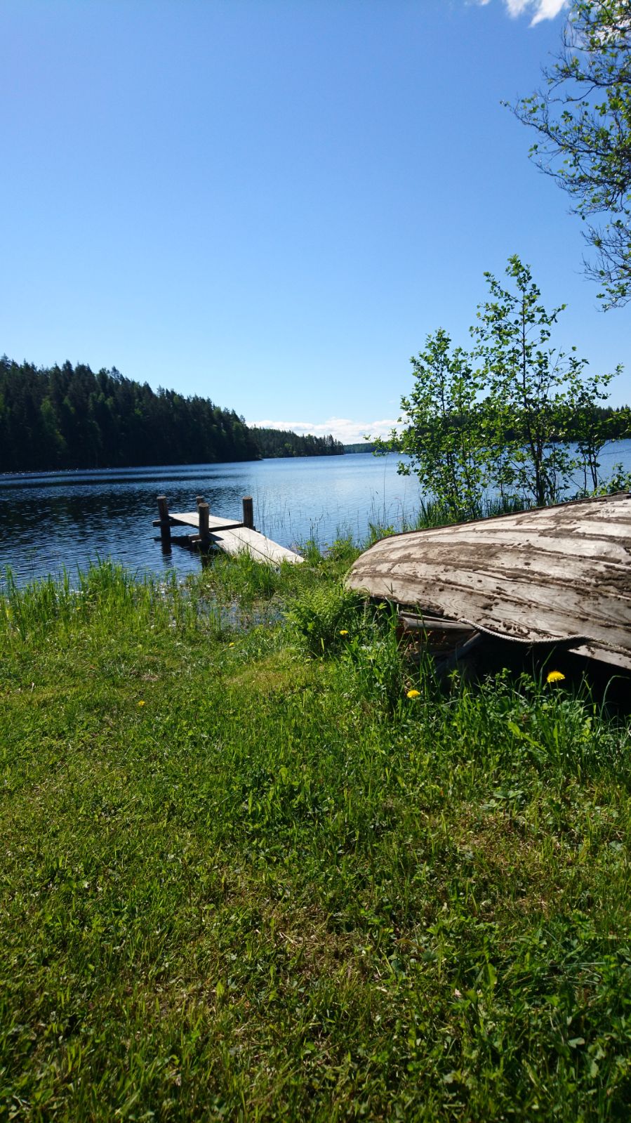 Kesäinen järvimaisema, rannallaan vene ja laituri.