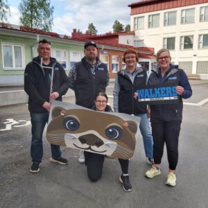 Pilvisenä päivänä Varkauden nuorisotalon edessä on viisi hymyilevää työntekijää, joista yksi pitelee kuvaa saukosta.