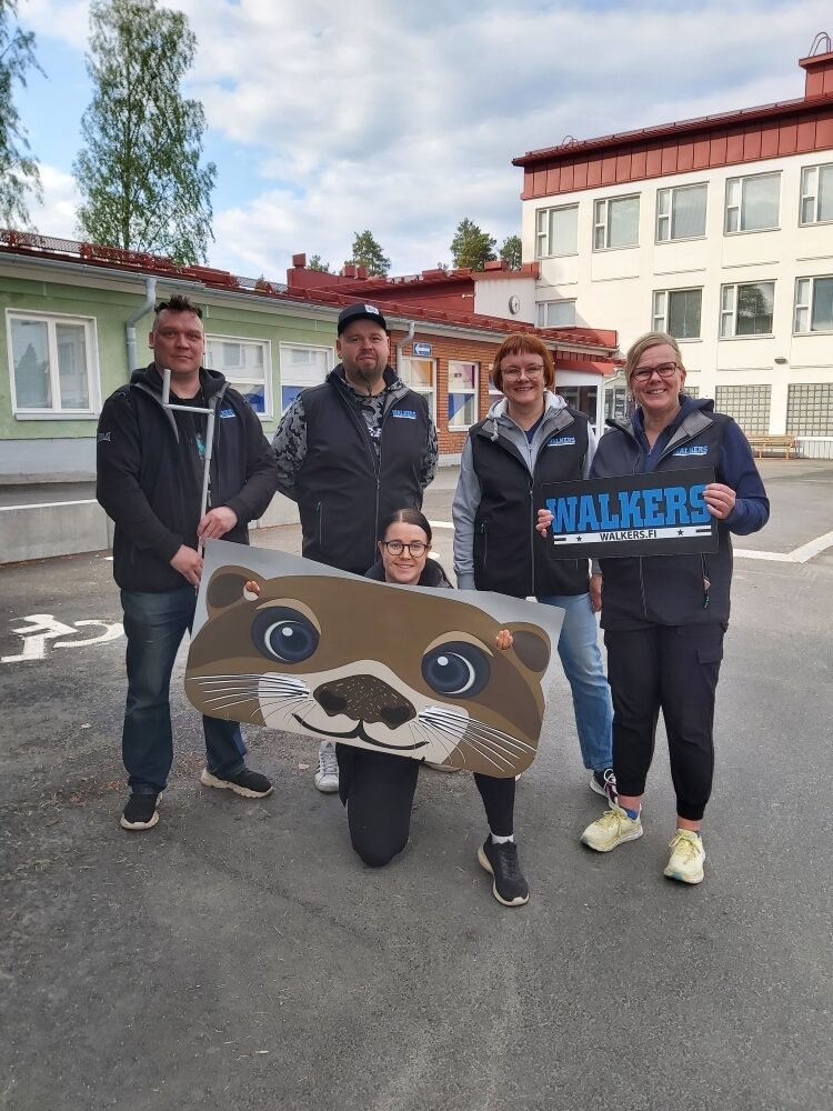 Pilvisenä päivänä Varkauden nuorisotalon edessä on viisi hymyilevää työntekijää, joista yksi pitelee kuvaa saukosta.