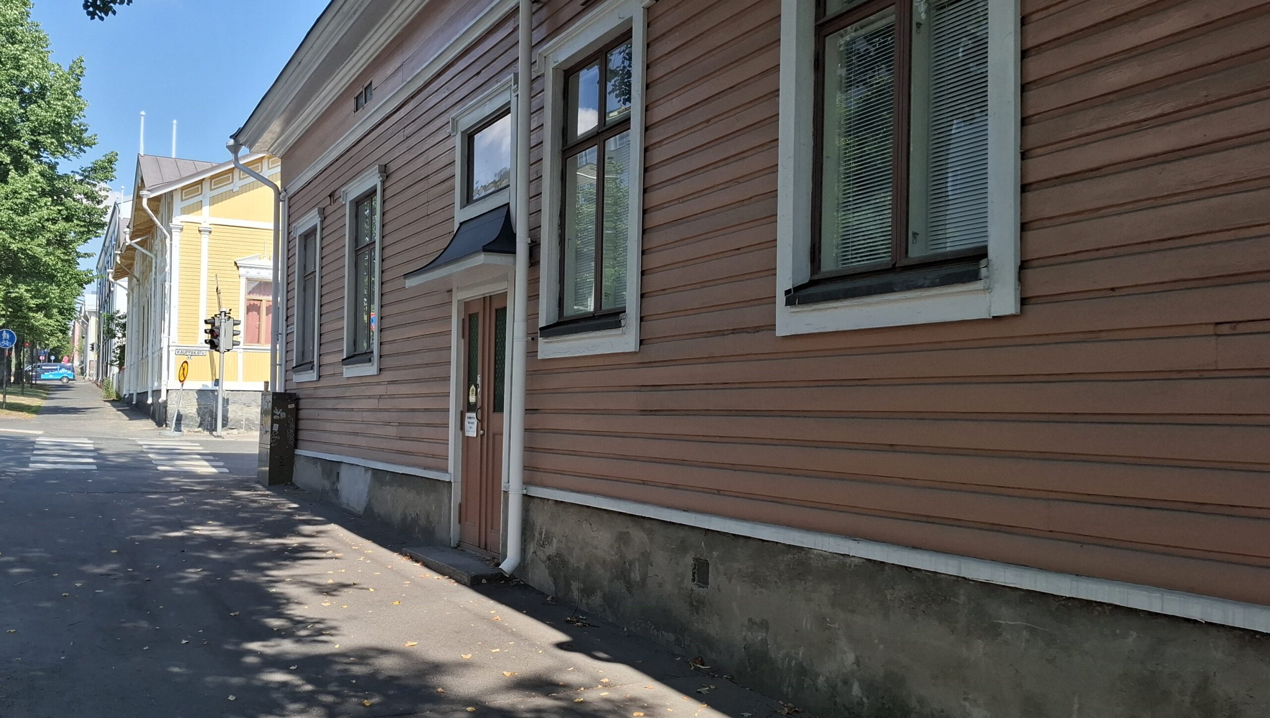 Vaaleanpunainen talo kadun varressa. Ovi keskellä taloa ja useampi ikkuna korkealla katutason yläpuolella.