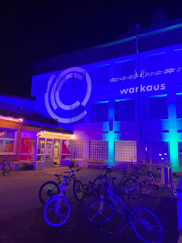 Kuva Nuorten Talosta etuoven puolelta, pihalla polkupyöriä ja pihavalaistuksia. Varkauden kaupungin logo heijastuu talon seinään.