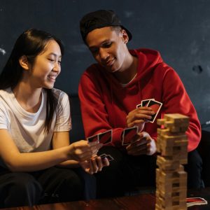 Nuoret pelaavat korttipeliä hymyillen. Pöydällä on myös Huojuva Torni -peli.