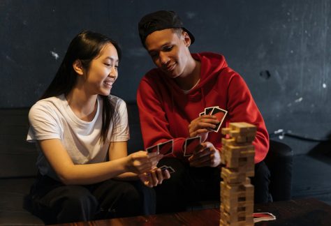 Nuoret pelaavat korttipeliä hymyillen. Pöydällä on myös Huojuva Torni -peli.