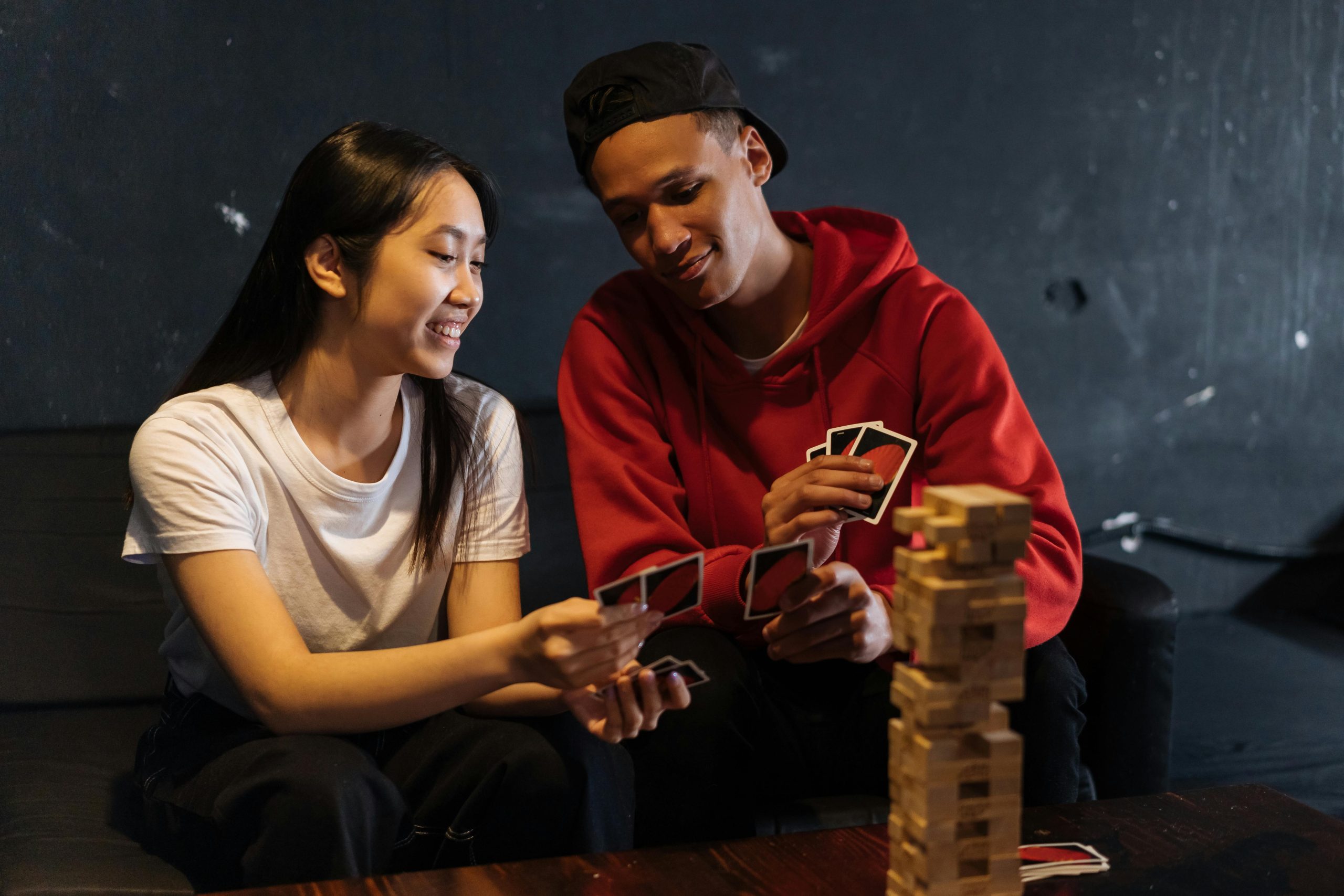 Nuoret pelaavat korttipeliä hymyillen. Pöydällä on myös Huojuva Torni -peli.