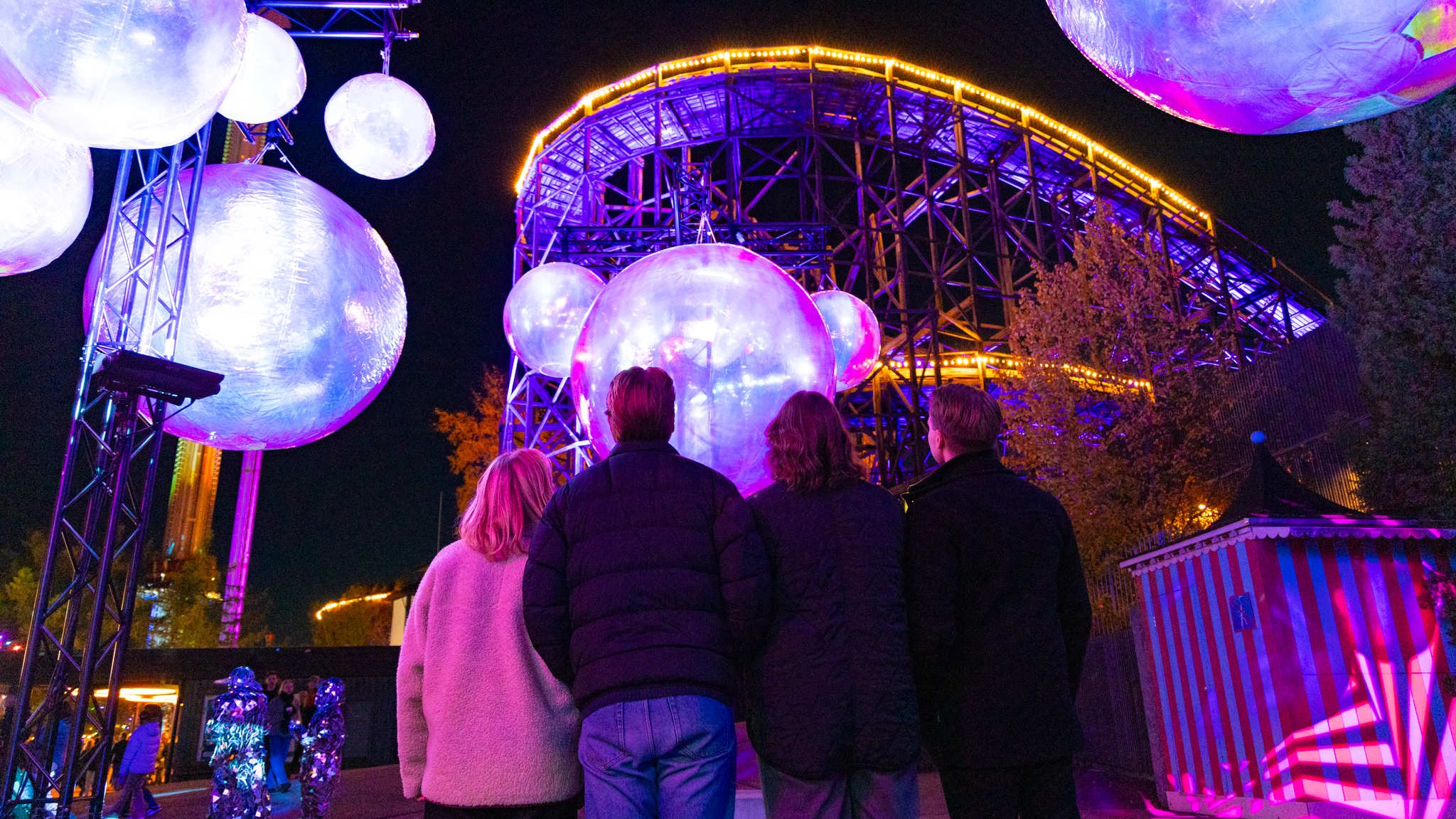 Ihmisjoukko katselemassa Linnanmäen huvipuistolaitteita valaistuina ja isoja vaaleita valopalloja.