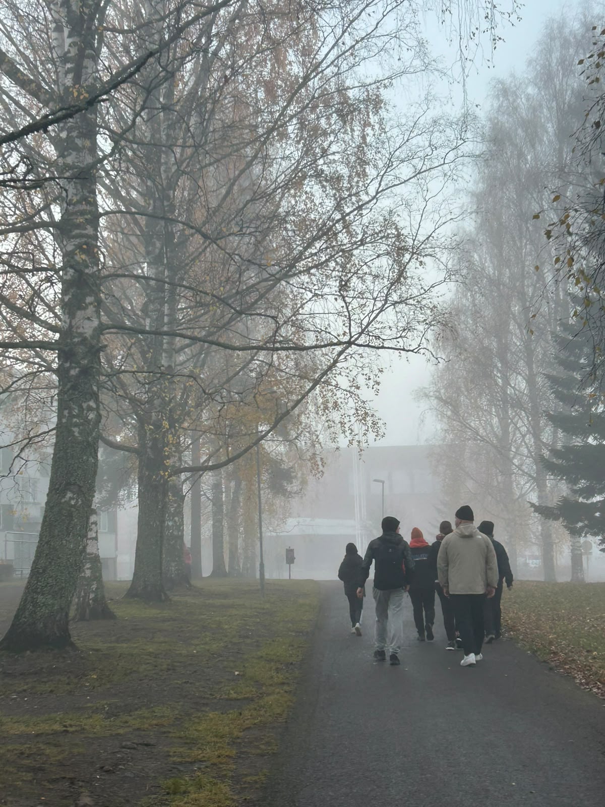 Ihmisiä kävelemässä kävelytiellä sumuisena syksyn iltana.